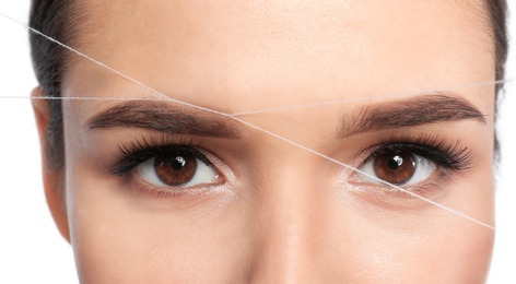 Young woman correcting eyebrow shape with thread, closeup