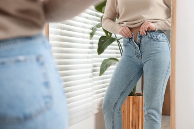 Woman in stylish jeans near mirror indoors, closeup