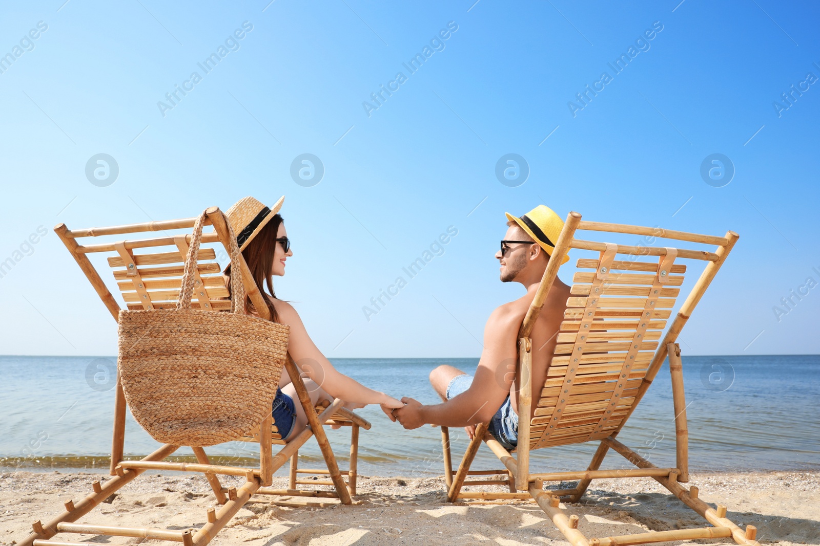 Photo of Young couple relaxing in deck chairs on beach