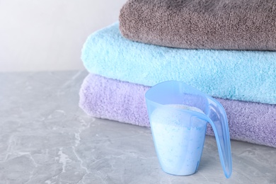 Photo of Clean towels and measuring cup of laundry powder on marble table against light background. Space for text