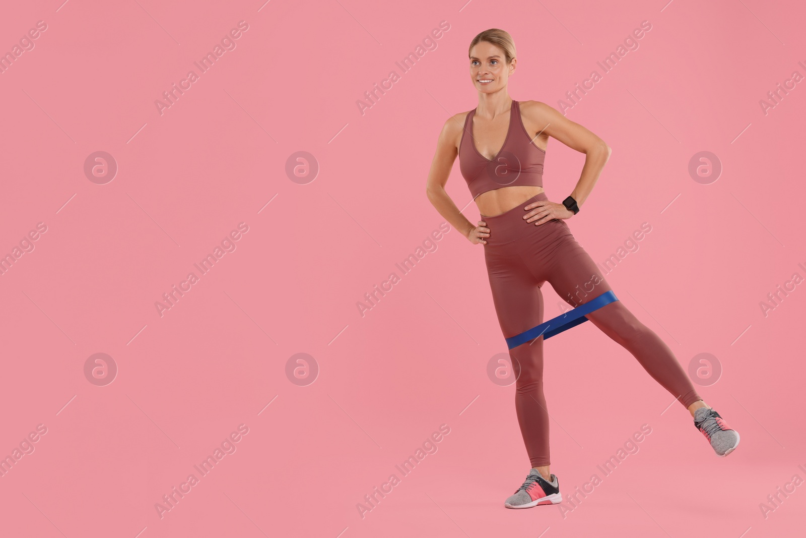 Photo of Woman exercising with elastic resistance band on pink background. Space for text