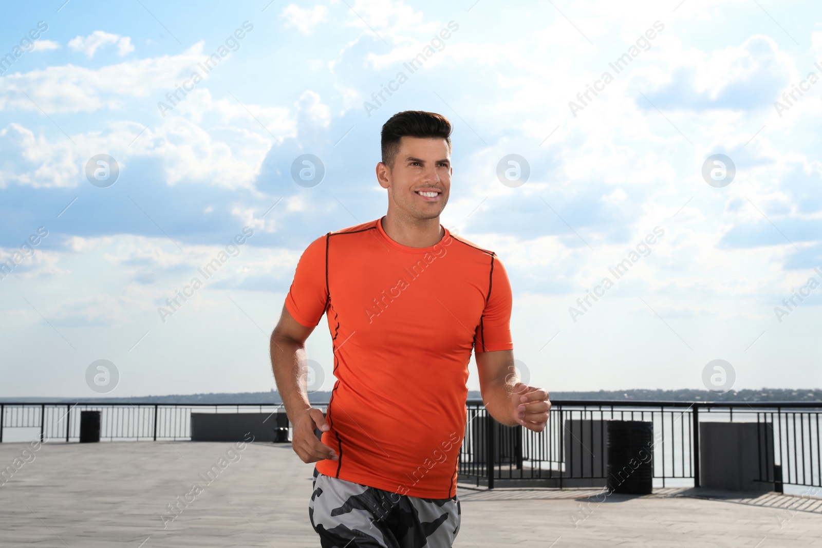 Photo of Handsome man in sportswear running outdoors on sunny day