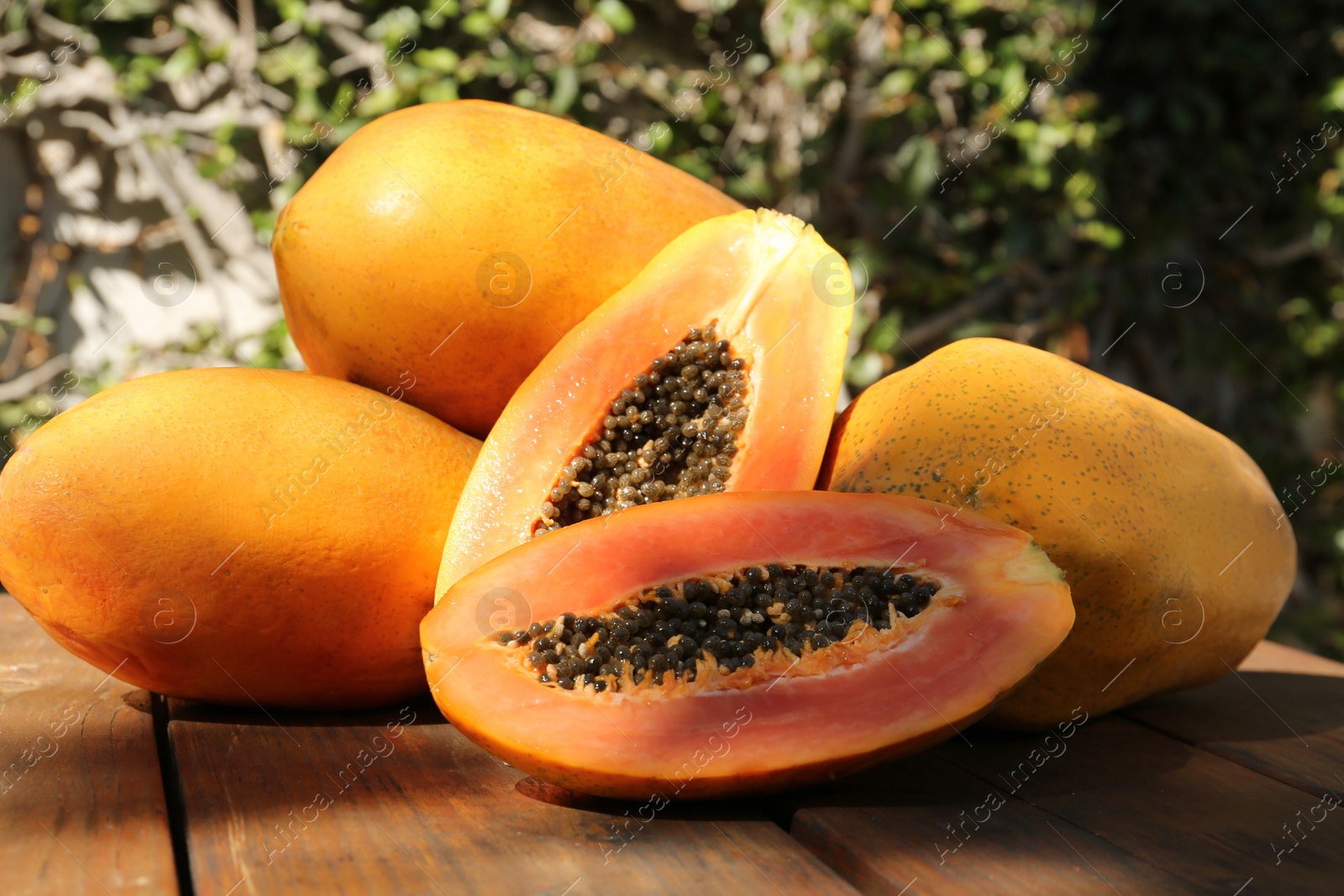 Photo of Fresh ripe cut and whole papaya fruits on wooden table outdoors