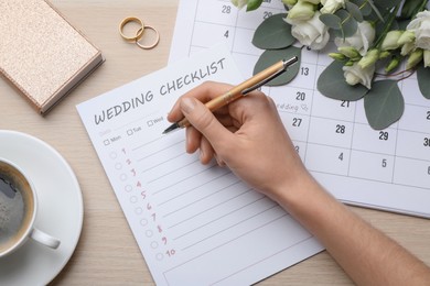 Photo of Woman filling Wedding Checklist at wooden table, top view