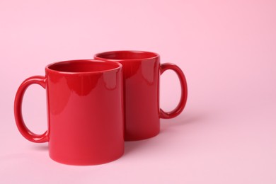 Photo of Two red ceramic mugs on pink background. Space for text