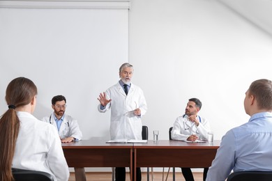 Senior doctor having discussion with audience during medical conference in meeting room
