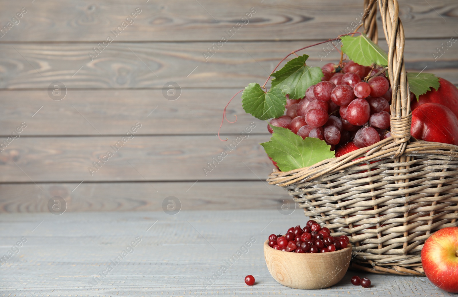 Photo of Wicker basket with fresh fruits and berries on grey wooden table. Space for text