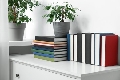 Photo of Many different books and potted plants on white cabinet indoors