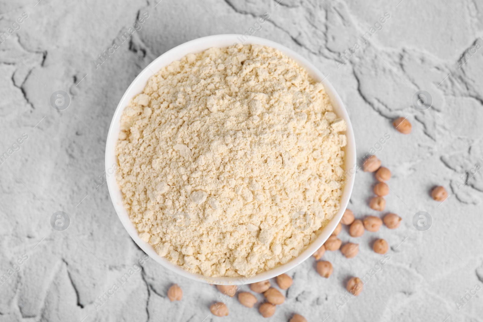 Photo of Chickpea flour in bowl and seeds on light grey textured table, top view