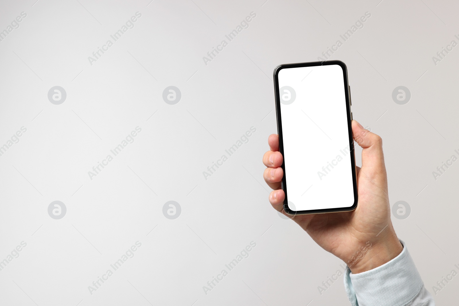 Photo of Man holding smartphone with blank screen on light grey background, closeup. Mockup for design