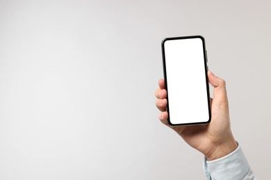 Man holding smartphone with blank screen on light grey background, closeup. Mockup for design