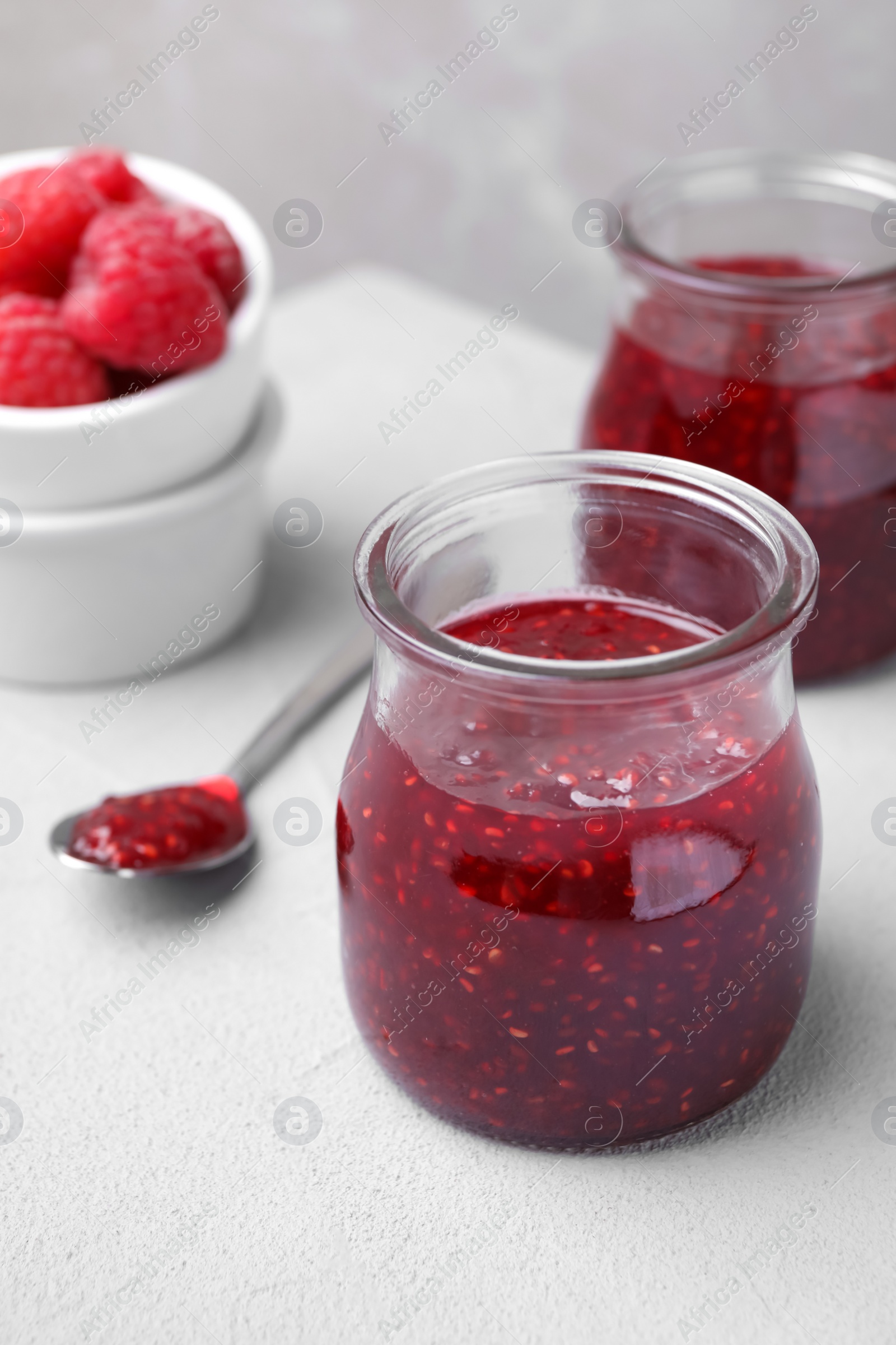 Photo of Delicious jam and fresh raspberries on light table