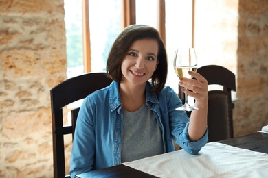 Photo of Woman with glass of white wine at table indoors