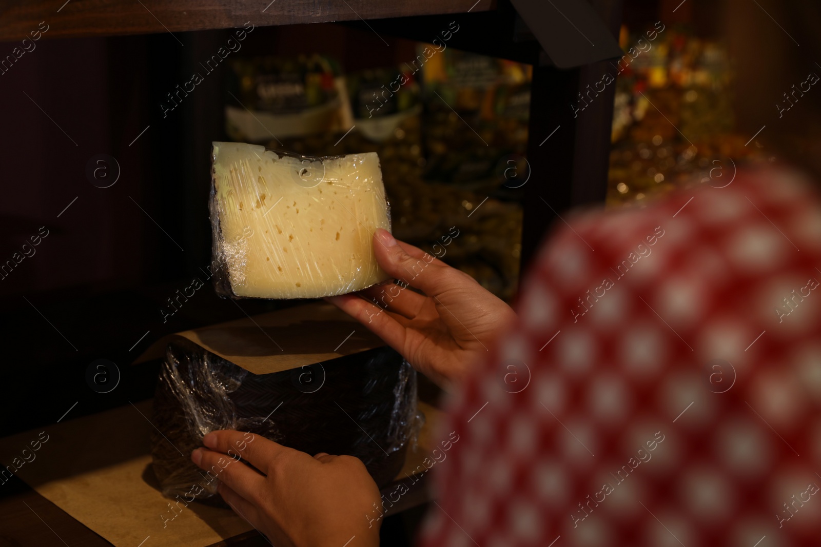 Photo of Woman choosing tasty cheese from display in store