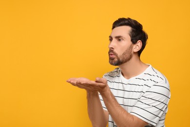 Photo of Handsome man blowing kiss on orange background. Space for text