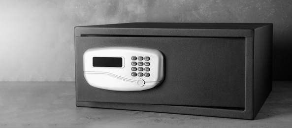 Image of Black steel safe with electronic lock on grey table, banner design