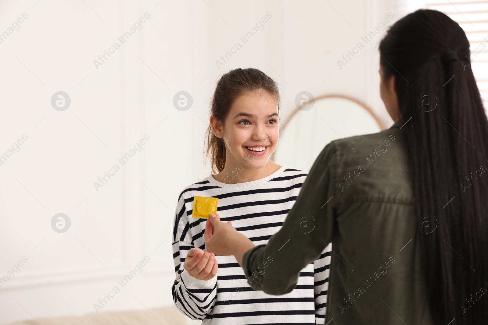 Photo of Mother giving condom to her teenage daughter at home. Sex education concept