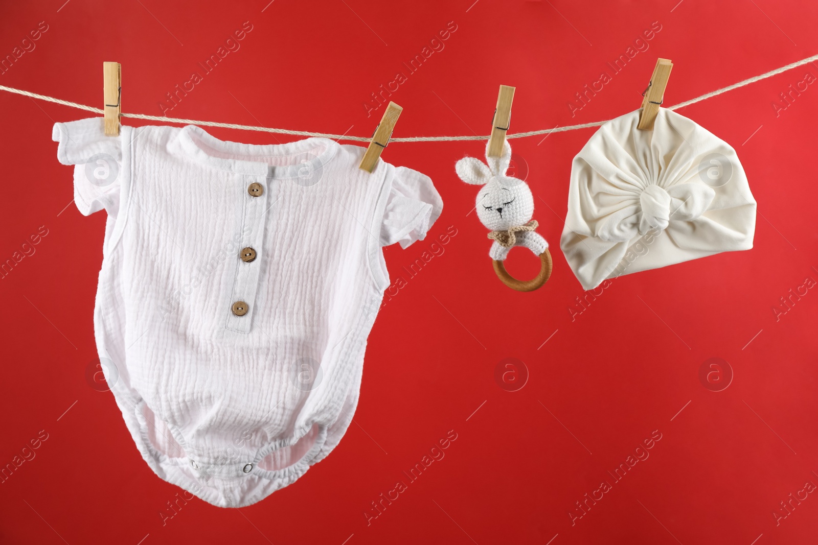 Photo of Baby clothes and accessories hanging on washing line against red background