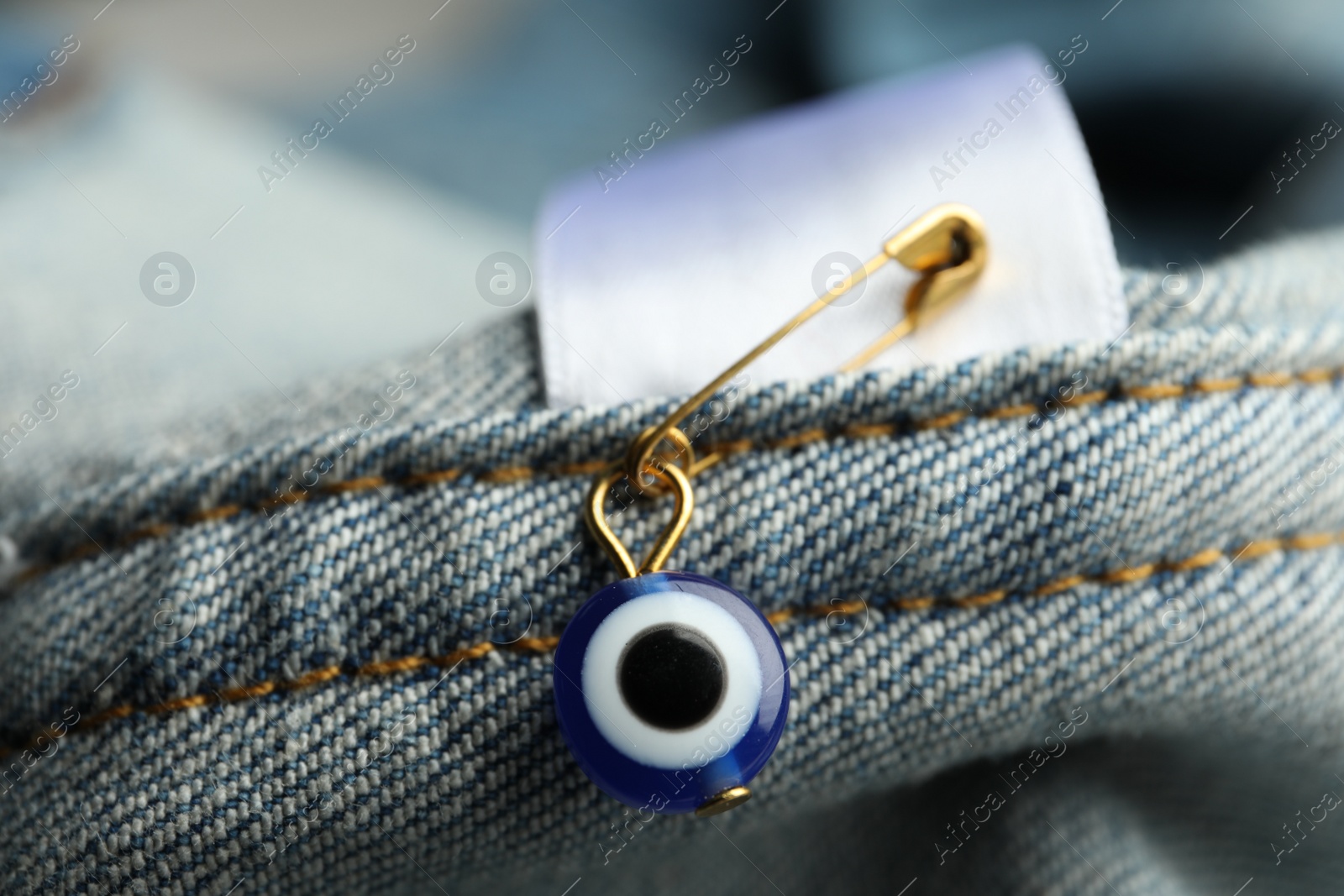 Photo of Evil eye safety pin on denim clothing, closeup