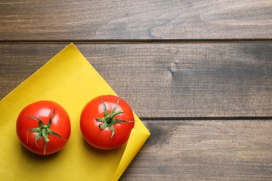 Photo of Fresh ripe tomatoes and waxed napkin on wooden table, top view. Space for text