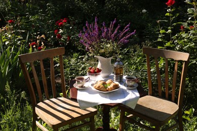 Beautiful bouquet of wildflowers, croissants and ripe strawberries on table served for tea drinking in garden