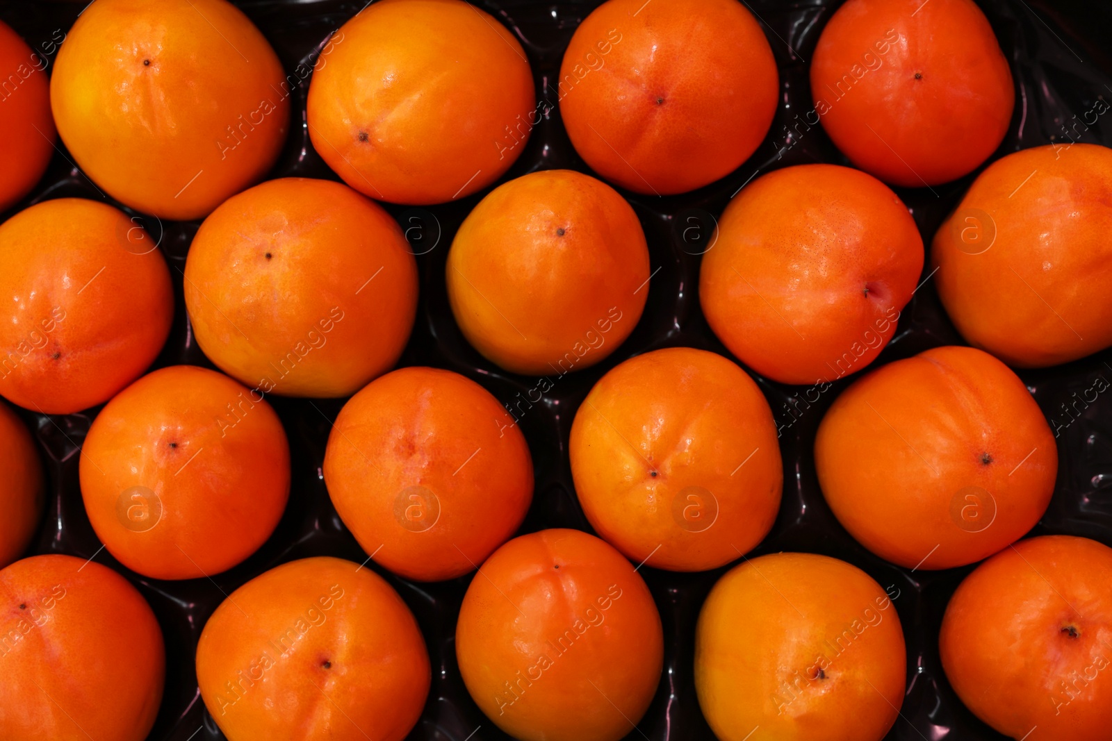 Photo of Many fresh persimmons in container at market, top view
