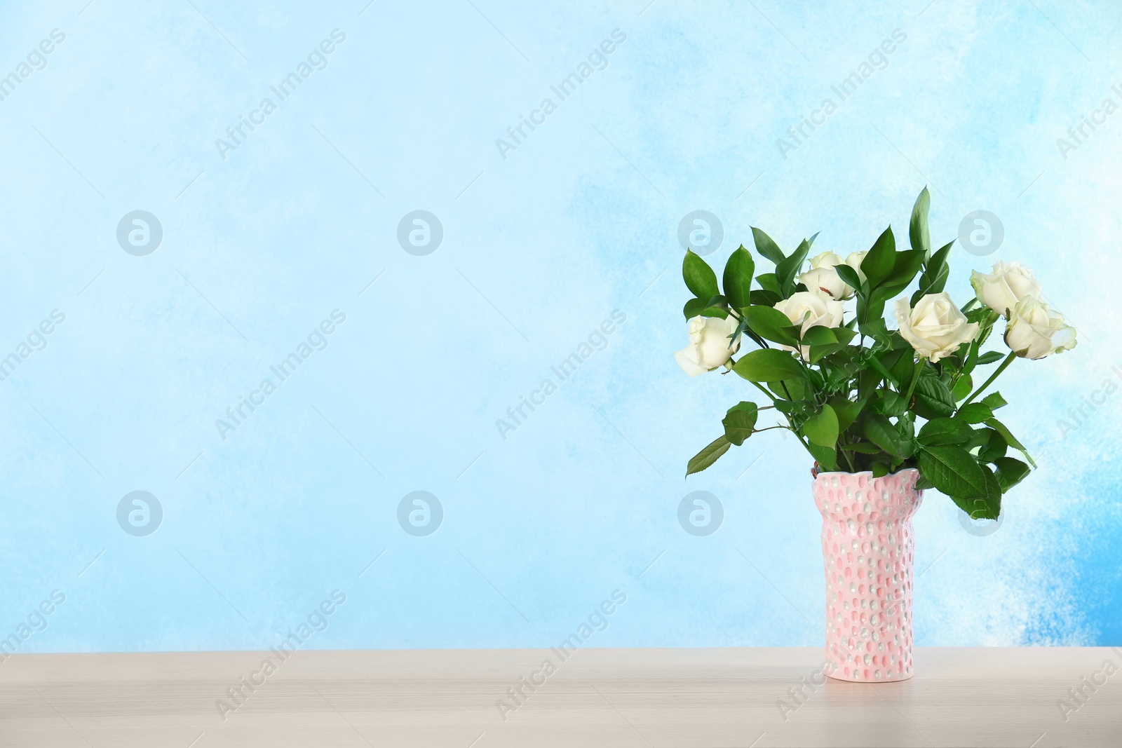 Photo of Vase with bouquet of beautiful roses on table against color background. Space for text