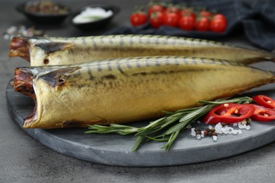 Photo of Delicious smoked mackerels and spices on dark grey table, closeup