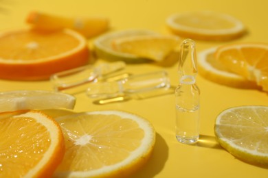 Skincare ampoules with vitamin C and citrus slices on yellow background, closeup