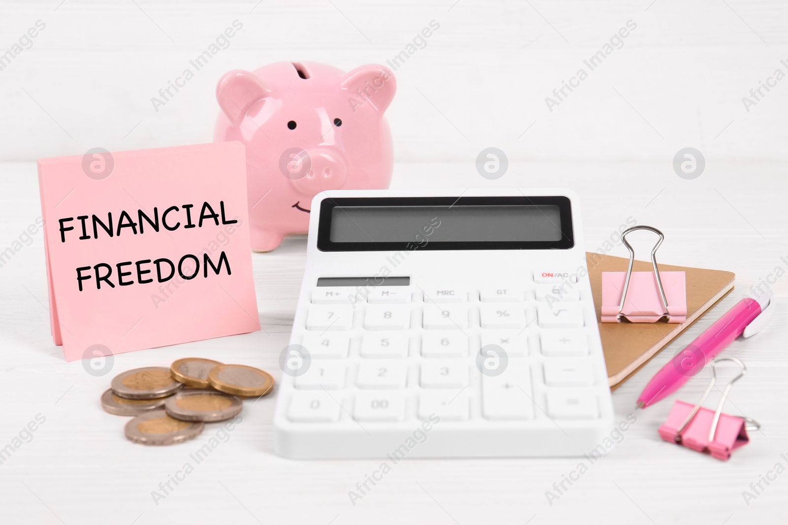 Image of Note with words Financial Freedom, calculator, coins, piggy bank and stationery on white table