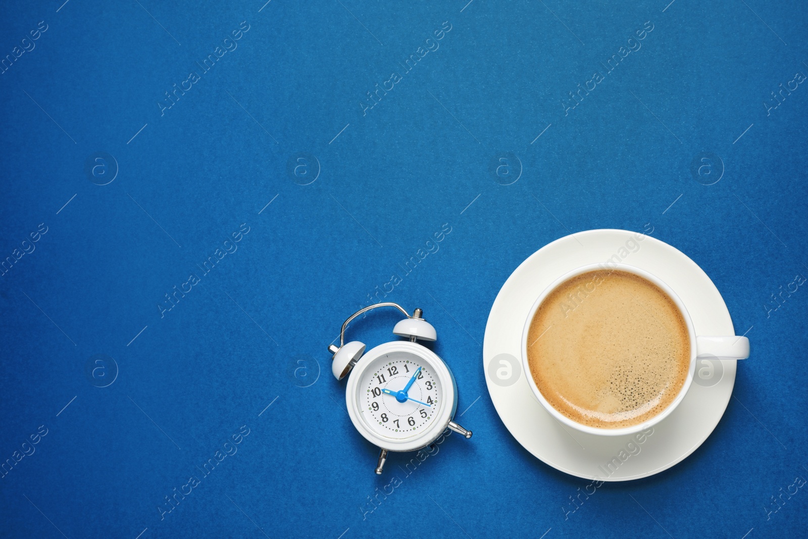 Photo of Classic black coffee and alarm clock on blue background, top view with space for text. Color of the year 2020