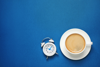 Photo of Classic black coffee and alarm clock on blue background, top view with space for text. Color of the year 2020