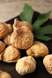 Photo of Tasty dried figs and green leaf on wooden board, closeup