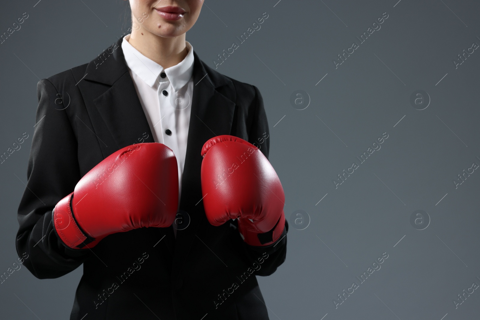 Photo of Businesswoman in suit wearing boxing gloves on grey background, closeup. Space for text
