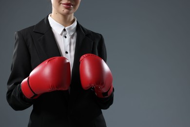 Businesswoman in suit wearing boxing gloves on grey background, closeup. Space for text