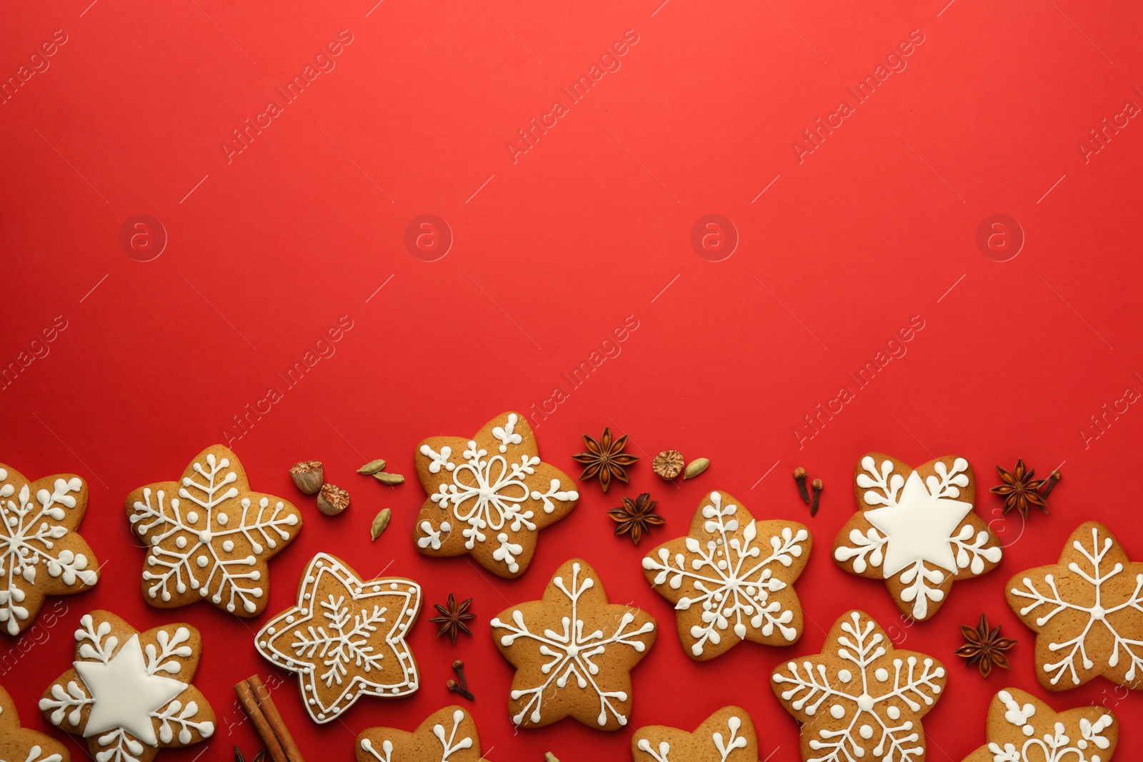 Photo of Tasty star shaped Christmas cookies with icing and spices on red background, flat lay. Space for text