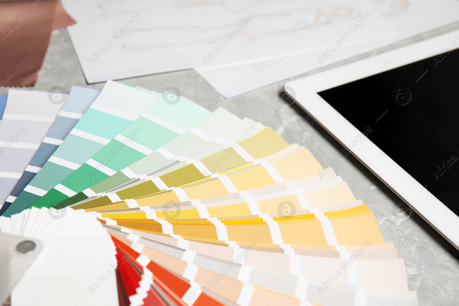 Photo of Palette samples and tablet on grey marble table, closeup. Designer's workplace