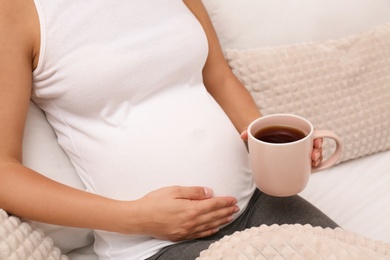 Pregnant woman drinking tea at home, closeup