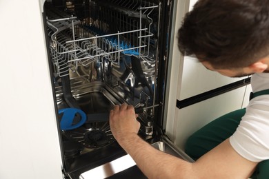 Photo of Serviceman repairing dishwasher with screwdriver indoors, closeup