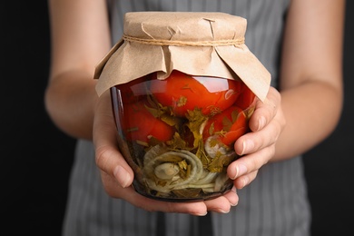 Photo of Woman holding glass jar with pickled tomatoes on black background, closeup view