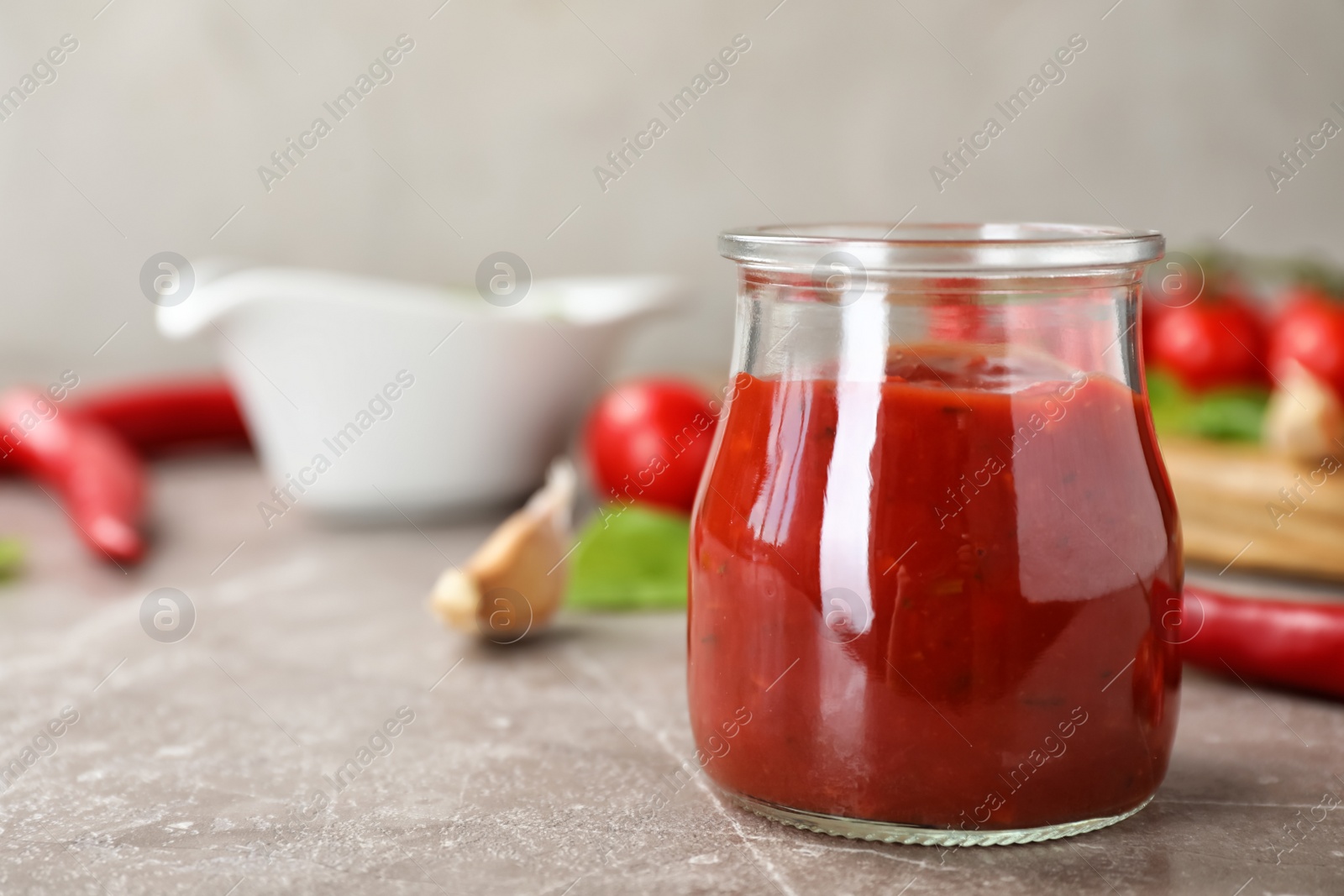 Photo of Jar with spicy chili sauce on gray table