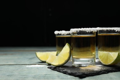 Photo of Mexican Tequila shots, lime slices and salt on blue wooden table. Space for text