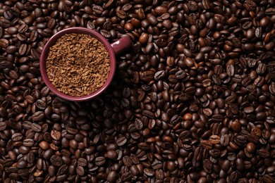 Photo of Cup with instant coffee on roasted beans, top view. Space for text