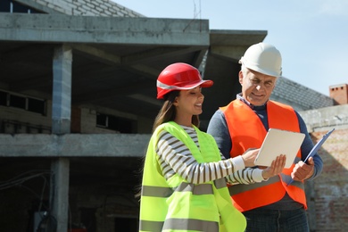 Photo of Professional engineer and foreman in safety equipment with tablet at construction site. Space for text