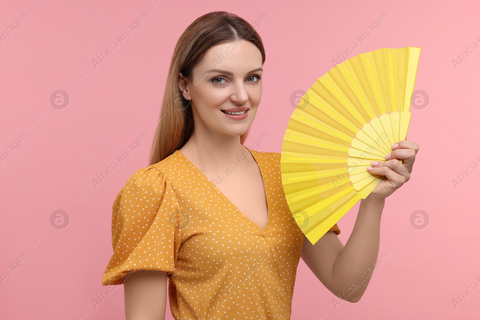 Photo of Happy woman with yellow hand fan on pink background