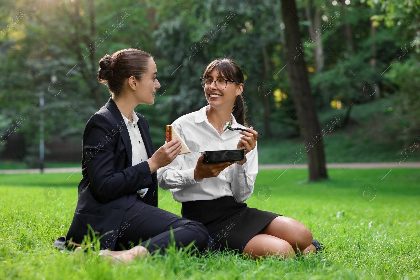 Photo of Happy colleagues having business lunch on green grass in park