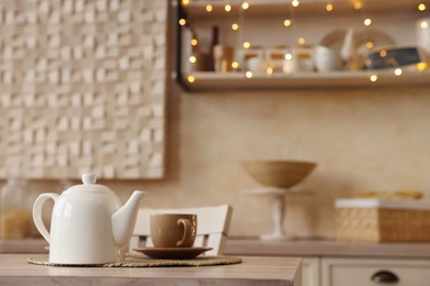 Photo of White teapot with cup on wooden table in kitchen, space for text