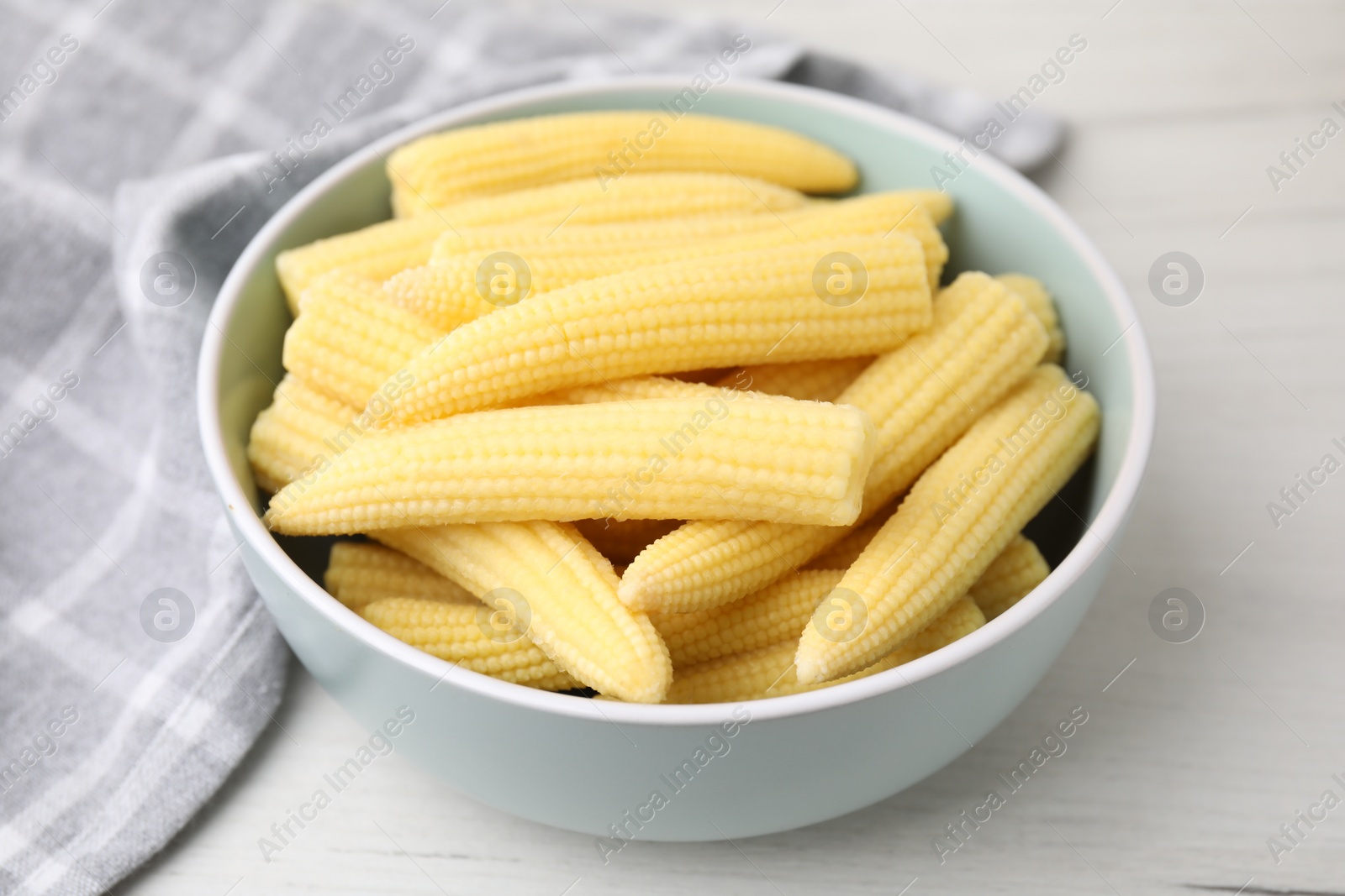 Photo of Tasty fresh yellow baby corns in bowl on white wooden table