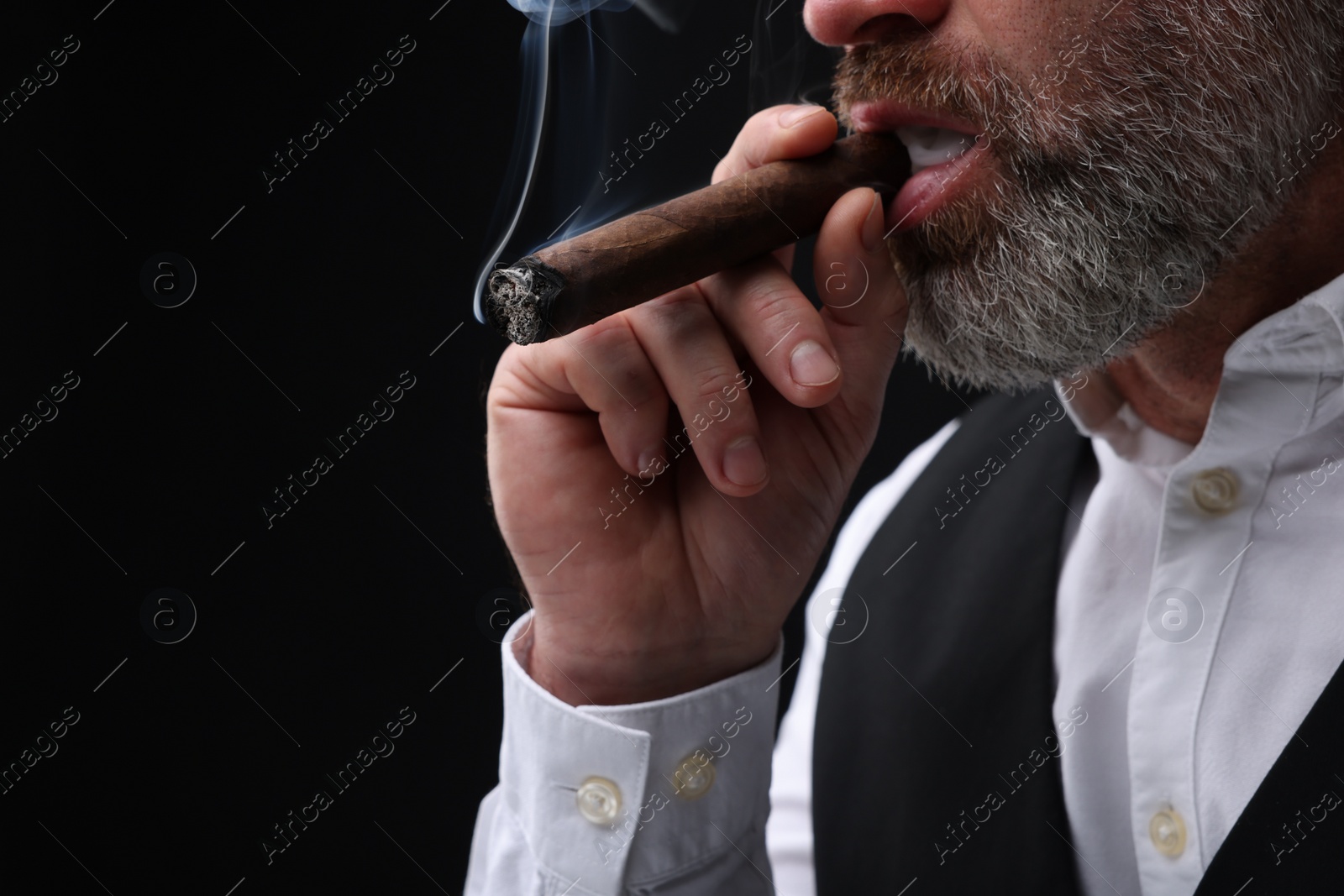 Photo of Bearded man smoking cigar against black background, closeup. Space for text