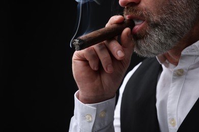 Bearded man smoking cigar against black background, closeup. Space for text